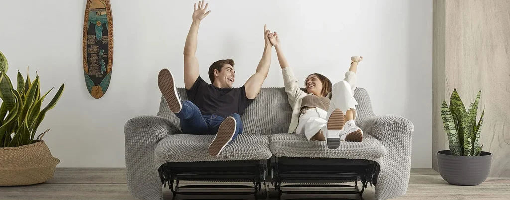 Pareja feliz disfrutando de un sofá relax cubierto con funda protectora elástica gris de ProtectSofa